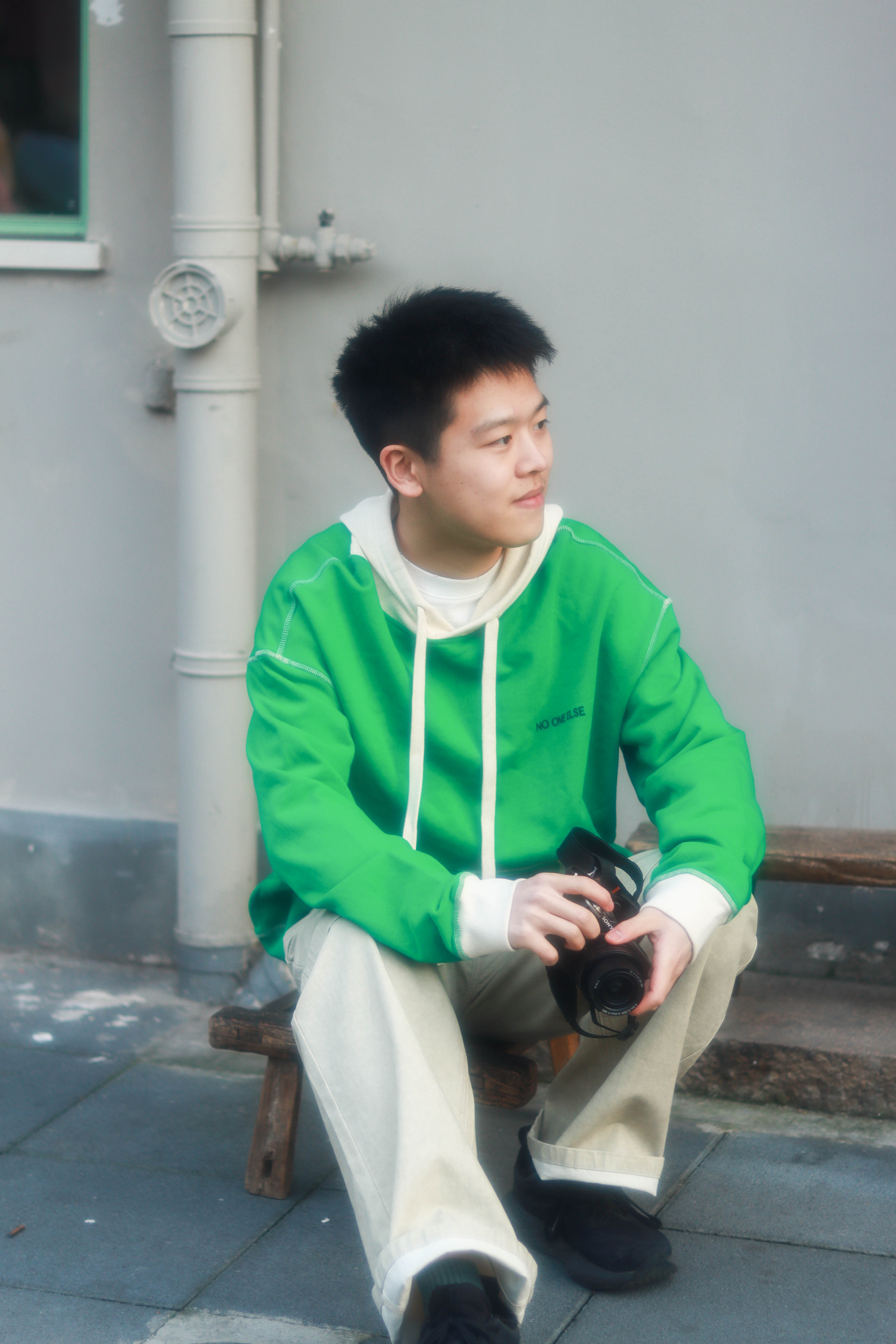 Toby sitting on a bench in a green hoodie, holding a camera.